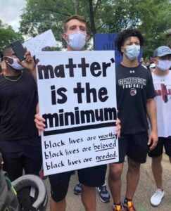 Group of Black Lives Matter Protesters with sign that says "'matter' is the minimum: black lives are worty, black lives are beloved, black lives are needed."